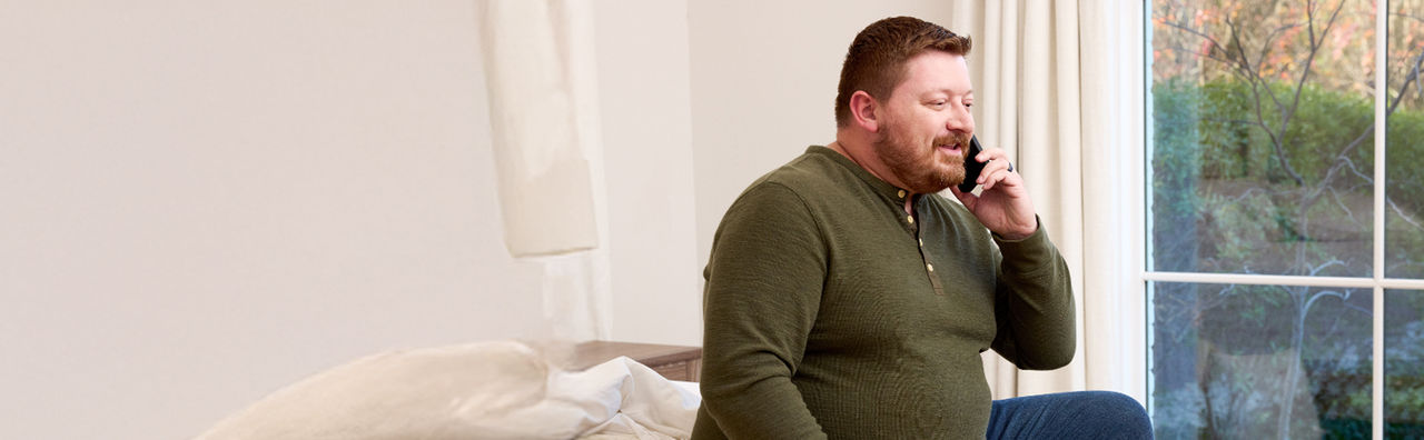 Man sitting in bedroom talking on cell phone.