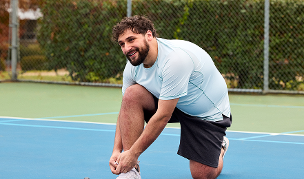Man lacing shoe on tennis court.