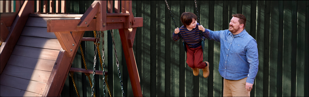 Man pushing child on swing set.