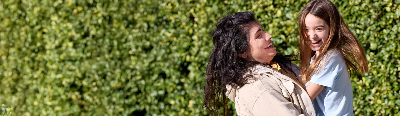 Woman smiling while holding child outdoors.